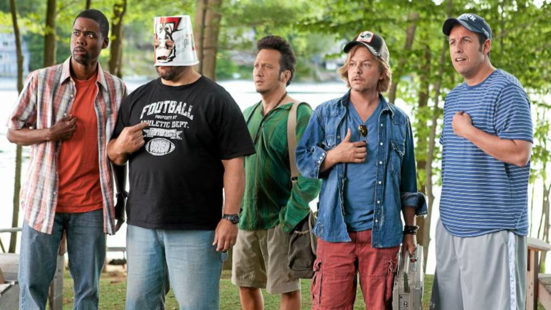 Five men stand by a lake with their hands on their chests, one wearing a bucket on his head. Scene from Grown Ups.