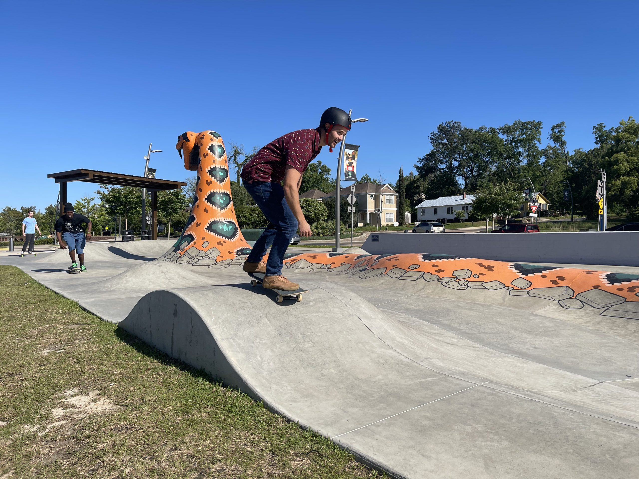 man skating over hill in skate park with concrete orange snake in the background
