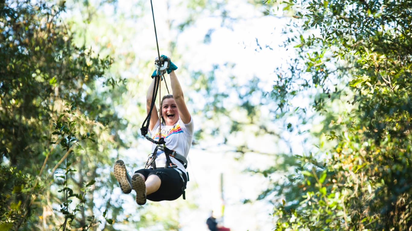 woman smiling while ziplining through trees
