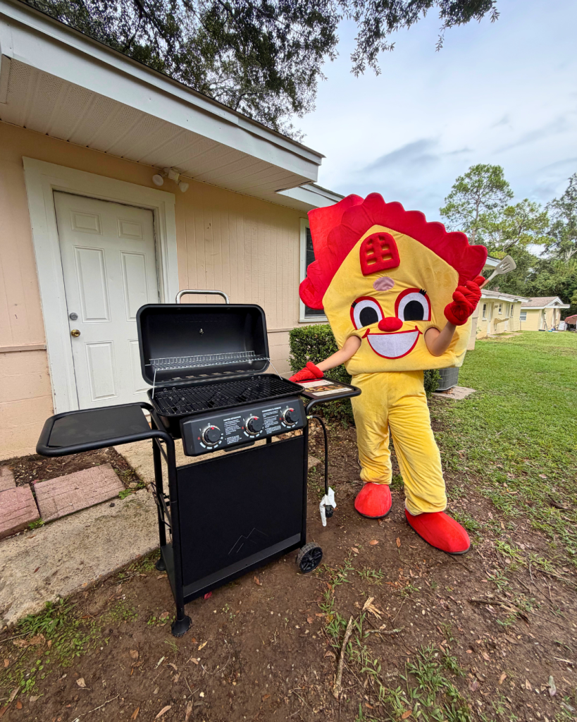 Photo of a house mascot posing next to a gas grill in the backyard of a house